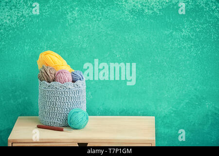 Basket with knitting yarn on table against color background Stock Photo