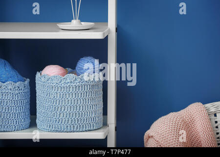 Baskets with balls of knitting yarn on shelf against color wall Stock Photo