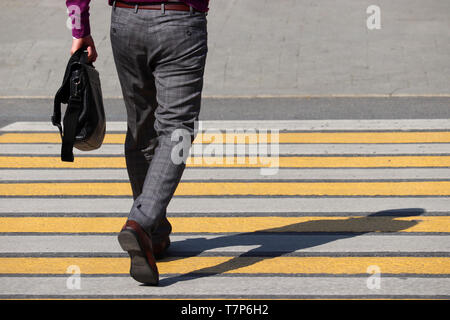 Stylish slender man in plaid pants walking on pedestrian crossing, shadow on zebra. Road marking, male legs on the crosswalk, street safety concept Stock Photo