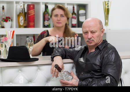 Elderly man with a bottle of whiskey in a cafe on the background of the waitress. Spirits lover. Bar customer and waitress Stock Photo