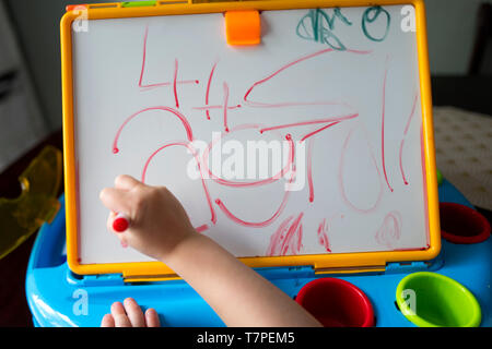 A four year old girl practices her handwriting on a whiteboard Stock Photo