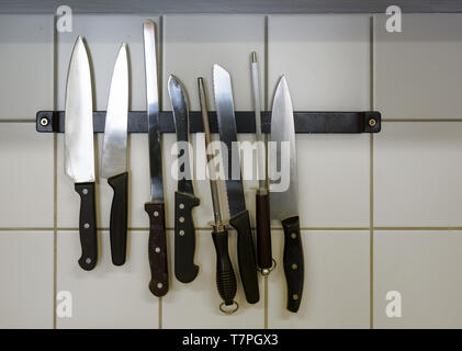 large kitchen knives and honing steels hanging on a magnetic holder on the tiled wall, copy space Stock Photo