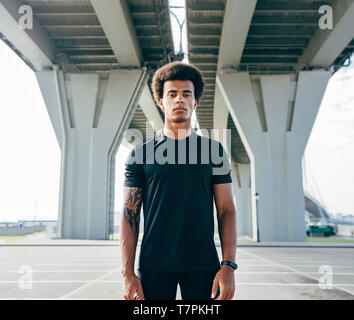 Young man in black sports clothes standing under a highway Stock Photo