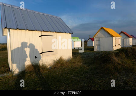 Shadow of a kissing couple on a white wooden cabin in a row of beach huts with colorful roofs at Gouville-sur-Mer, Normandy, France Stock Photo