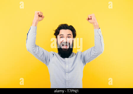 Excited bearded man standing with fists up over yellow  background, the concept of joy in winning Stock Photo