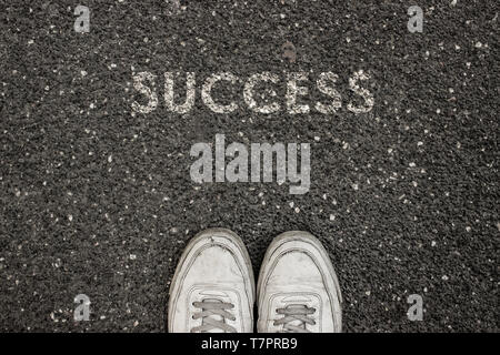 New life concept, Sport shoes and the word SUCCESS written on asphalt ground, Motivational slogan. Stock Photo