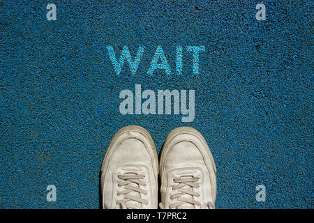 New life concept, Sport shoes and the word WAIT written on blue walk way ground, Motivational slogan. Stock Photo