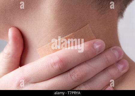 Adhesive plaster on the neck of a teenager on a wound. Hand touches a sore spot. Stock Photo