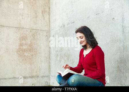 A young woman sitting crossed legged outside reading a book, Edinburgh Scotland. Stock Photo