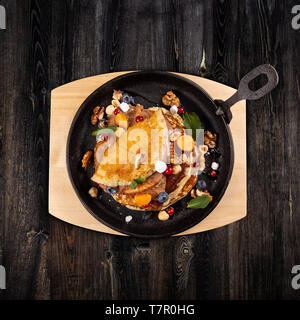 Delicious sweet pancakes served on a cooking pan with fresh fruits, nuts and chocolate sauce Stock Photo