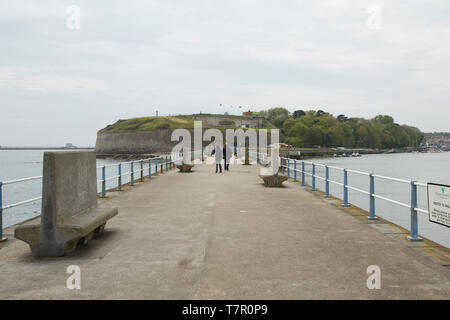 A view looking shorewards of the Stone Pier and the Nothe Fort in the background with two people walking down pier. Weymouth Dorset England UK GB. Stock Photo