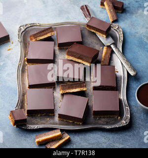 Chocolate caramel slices, bars, millionaires shortbread on a vintage tray. Blue background. Stock Photo