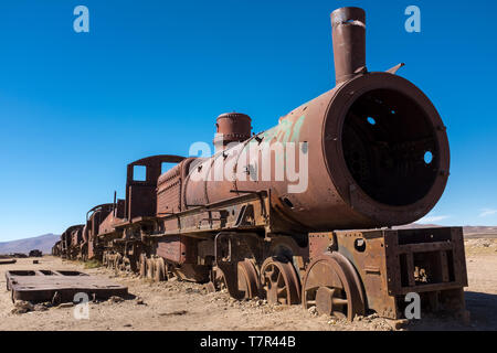 A head on shot a rusting steam trains and carriages  that are slowly rot away at the train graveyard just outside of Uyuni, Bolivia, against a bright blue sky. Stock Photo