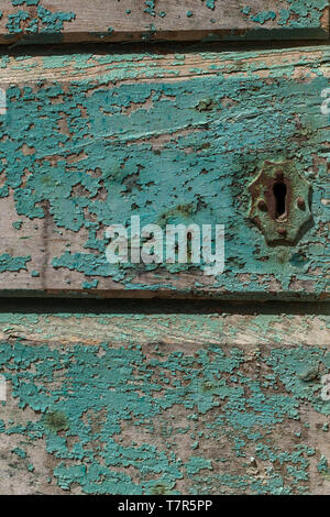 A close up of a rusting key hole on a painted slated wooden door, the aqua blue paint is faded and peeling away Stock Photo