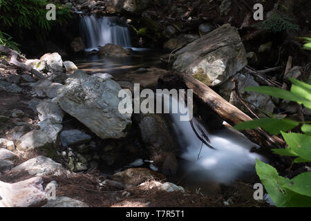 A small multi-tiered waterfall with rocks and green foliage, long exposure shot to smooth out the cascading water Stock Photo