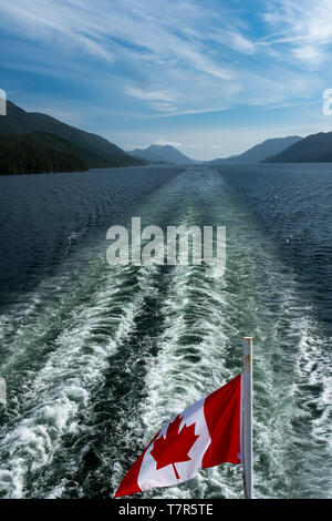 The Canadian flag flying in the wind at the back of ferry as the boat makes it way through the Inside Passage with the wake, portrait aspect  Stock Photo
