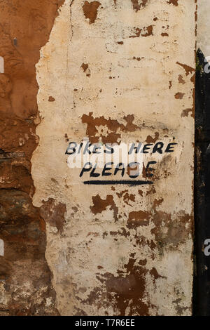 A close up of a hand painted sign on where to leave your bike on an exposure brick wall with the plaster falling away Stock Photo