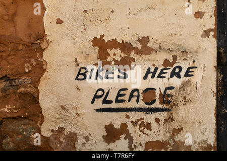 A close up of a hand-painted sign on where to leave your bike on an exposed brick wall with the plaster falling away Stock Photo