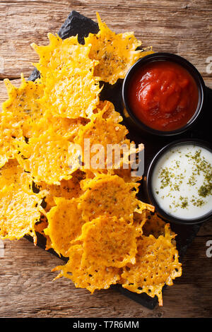 Fried cheddar cheese chips with herbs served with sauces close-up on the table. Vertical top view from above Stock Photo