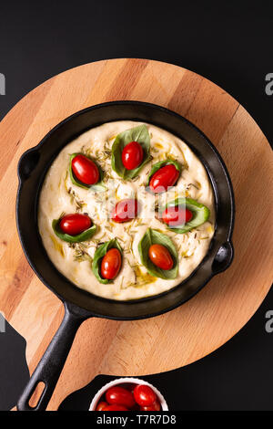 Food concept rising dough for Homemade organic Focaccia in skillet iron pan on black background with copy space Stock Photo