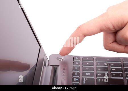 Close-up view of female hand with index finger, pushing start button of silver laptop with black keyboard and display. Turns the notebook on or off. I Stock Photo