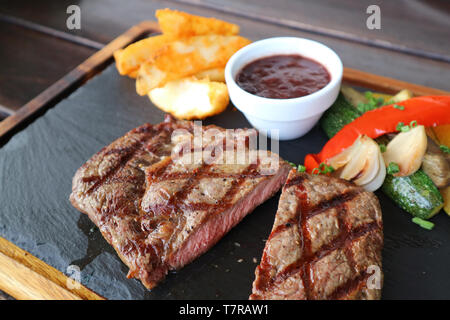 Cut medium grilled ribeye steak with red wine sauce and saute vegetables on hot stone plate Stock Photo