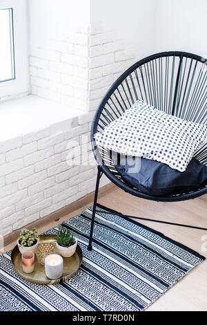 Bright white apartment interior decor, candles and plants on vintage tray with pillows in chair and carpet on the floor Stock Photo
