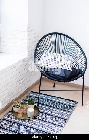 Bright white apartment interior decor, candles and plants on vintage tray with pillows in chair and carpet on the floor Stock Photo