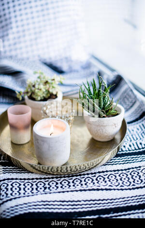 Real apartment interior decor, aromatic candles and plants on vintage tray with pillows and blanket on white windowsill Stock Photo
