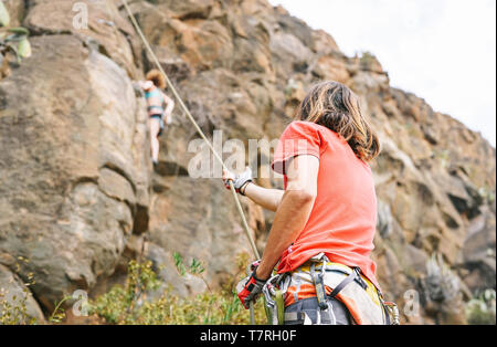Man giving assistance to woman who is climbing up on mountain cliff - Climbers in action on high rock  - concept of extreme sport lifestyle people Stock Photo