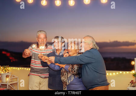 Happy senior friends celebrating birthday with sparklers stars outdoor - Older people having  fun in terrace in the summer nights Stock Photo