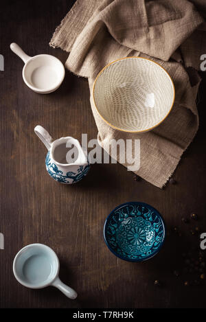 Vertical photo of few ceramic bowls with various shapes and colors. Bowls are placed on dark wooden vintage board. One bowl is placed on light brown c Stock Photo