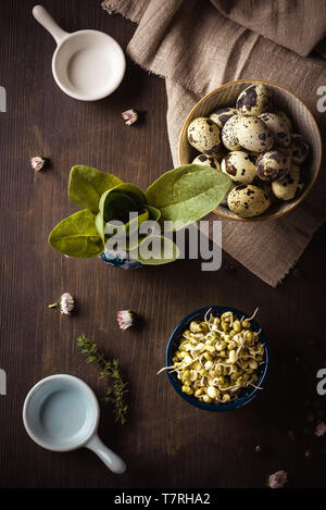 Vertical photo with top view on vintage wooden board with several bowls which contain mung bean sprouts, quail eggs and spinach. Light cloth is under  Stock Photo