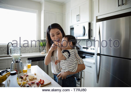 Mother feeding toddler daughter in kitchen
