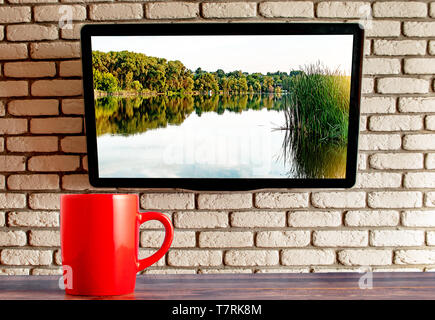 red cup on the table TV on the wall of decorative brick in the background Stock Photo