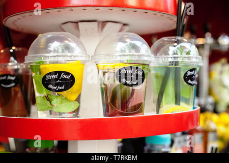 Plastic drinking disposable cups with refreshing fruit drinks and mint leaves sale on street market. Infused water with lemons and herbs Stock Photo