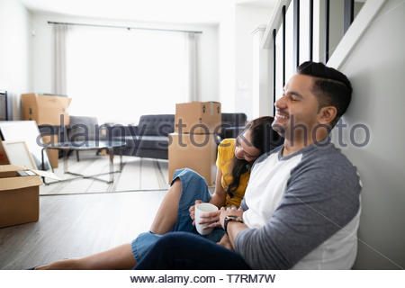 Affectionate, happy couple taking a break from moving, drinking coffee on floor