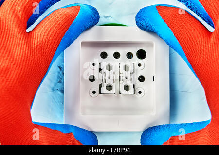 Worker in protective gloves is putting cover on new push button, electric installation work. Stock Photo