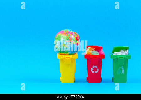 Ecology problem of environmental pollution planet, consumerism, recycling concept. Mini recycle bins containers with globe on blue background. Stock Photo