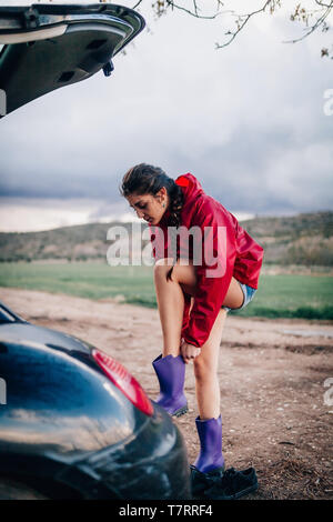 Girl putting her waterproof boots near her car. Stock Photo