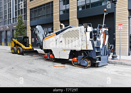 Road work equipment consisting of a small skidsteer loader and a road reclaimer parked at the side of an under-construction road in a city. Stock Photo