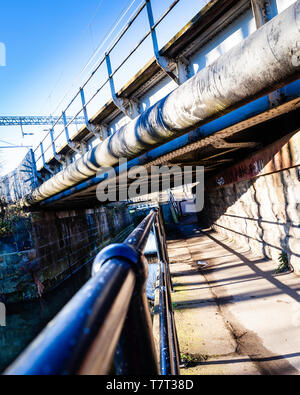 Canal towpath under a large pipe, and railway bridge. Stock Photo