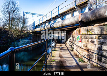 Towpath under a large pipe, and railway bridge. Stock Photo