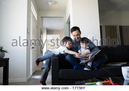 Father and toddler children reading book on living room sofa