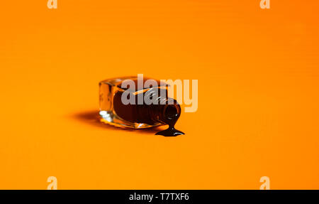 Dark nail polish spilled from the bottle. Vibrant trendy orange background. Stock Photo