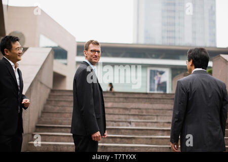 Portrait of a mid-adult businessman standing with two male colleagues in front of a flight of stairs the city. Stock Photo