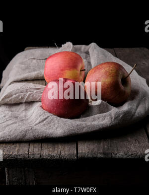 three fresh red apples lay on gray linen napkin, dark background Stock Photo