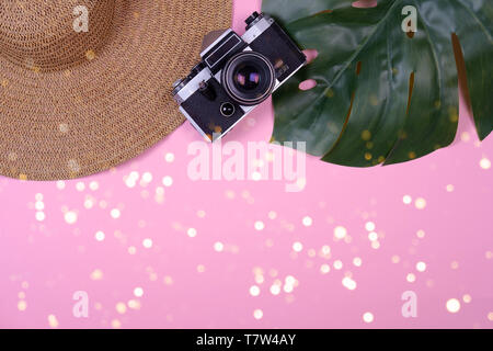 Women's traveler accessories: straw hat, tropical leaf monstera, retro camera on pink background with bokeh lights. Concept of travel with copy space. Summer background. Flat lay, overview Stock Photo