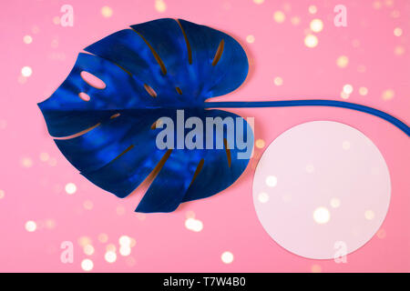 Vibrant bold blue tropical monstera leaf on pink background with copy space and with bokeh lights. Art neon surrealism concept Stock Photo