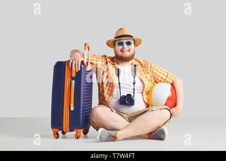 Fat funny man with a suitcase smiling on a gray background. Stock Photo